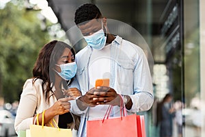 Portrait of black couple using smartphone wearing masks near mall