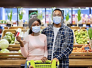 Portrait of black couple wearing protective masks and holding credit card at shopping mall during coronavirus pandemic