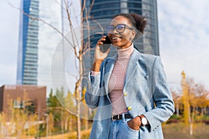 Portrait of a black ethnic businesswoman wearing glasses in a business park having a phone call