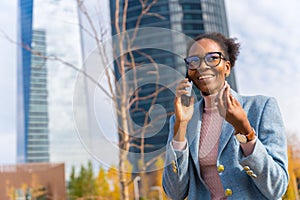 Portrait of a black ethnic businesswoman wearing glasses in a business park having a phone call