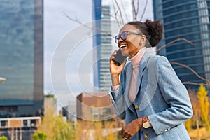 Portrait of a black ethnic businesswoman wearing glasses in a business park having a phone call