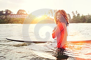 Portrait of black long-haired teen boy with surfboard ready for surfing with sunset backlight. He walking in Indian ocean waves.
