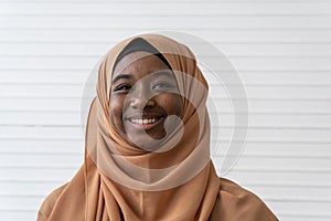 Portrait of Black muslim girl in Brown Hijab with smiling face with White wall in background