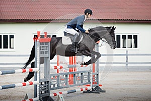 Black stallion horse and handsome man rider jumping obstacle during showjumping competition photo