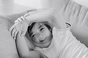 Portrait black and white image of happy young boy looking at camera with smiling face, Positive child lying on sofa relaxing at