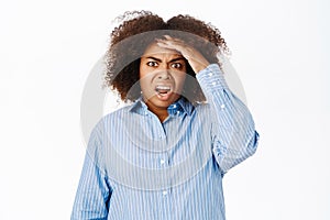 Portrait of black woman looking shocked and concerned at camera, gasps startled, stands over white studio background