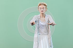 Portrait of blind young blonde woman in white shirt, skirt, and striped blouse standing, with closed eyes and trying to touch or