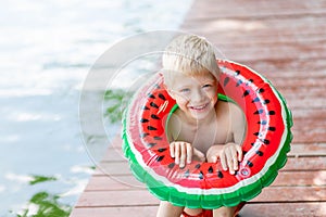 Portrait of a blond boy with a circle in the form of a watermelon in summer, a child`s vacation in the village, a happy childhood