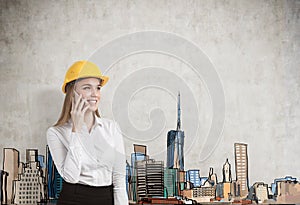 Portrait of a blond businesswoman wearing a yellow hard hat and talking on her smartphone.