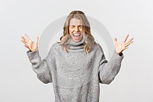 Portrait of blond girl in casual grey sweater losing control over emotions, screaming and shaking hands distressed