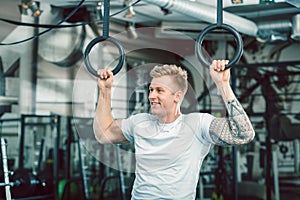 Handsome young man with strong arms hanging on gymnastic rings