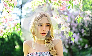 Portrait of blond lady with long curled hair and blue eyes in floral garden. Girl in vintage style outfit enjoying warm