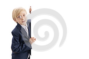 Portrait of blond little boy with white blank background. Boy with glasses peeking out from behind board. Copy space. Isolated