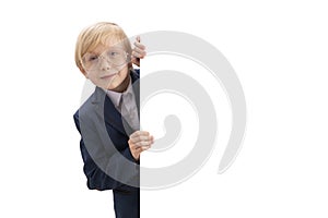 Portrait of blond little boy with white blank background. Boy with glasses and school uniform peeking out from behind board.