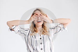 Portrait of blond pretty woman wearing wrist watch smiling and covering her eyes with hands