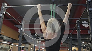 Portrait of blond sportswoman, who is doing chin-ups on bar in modern gym.