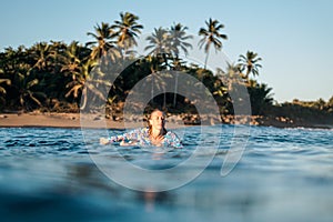 Portrait of blond surfer girl on white surf board in blue ocean pictured from the water in Encuentro beach photo