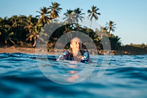 Portrait of blond surfer girl on white surf board in blue ocean pictured from the water in Encuentro beach photo