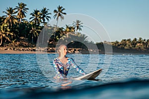 Portrait of blond surfer girl on white surf board in blue ocean pictured from the water in Encuentro beach photo