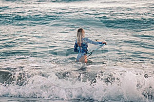 Portrait of blond surfer girl with white surf board in blue ocean pictured from the water in Encuentro beach photo