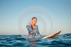 Portrait of blond surfer girl on white surf board in blue ocean pictured from the water in Encuentro beach photo