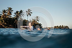 Portrait of blond surfer girl on white surf board in blue ocean pictured from the water in Encuentro beach photo