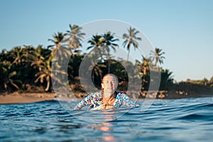 Portrait of blond surfer girl on white surf board in blue ocean pictured from the water in Encuentro beach photo