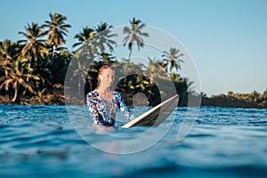 Portrait of blond surfer girl on white surf board in blue ocean pictured from the water in Encuentro beach photo