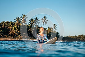 Portrait of blond surfer girl on white surf board in blue ocean pictured from the water in Encuentro beach photo