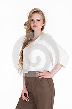 Portrait of blond woman with long hair looking at camera, dressed in white blouse and brown trousers