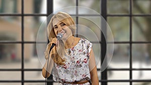 Portrait of a blond woman singing in microphone indoors.