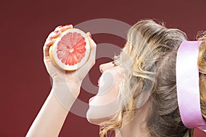 Portrait of Blond Woman Squeezing Grapefruit Half To Her Mouth.