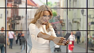 Portrait of a blond woman taking a selfie indoors.