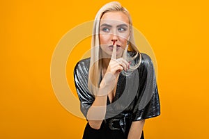 Portrait of a blond young woman asking to be quieter on a yellow studio background