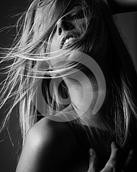 Portrait of blond young woman with beautiful makeup and flying wild hair in black lace dress stands on gray background