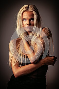 Portrait of blond young woman with beautiful makeup and hairstyle in a black lace dress stands on gray background