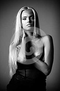 Portrait of blond young woman with beautiful makeup and hairstyle in a black lace dress stands on gray background