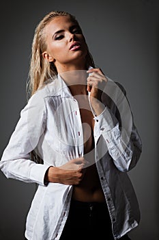 Portrait of blond young woman with beautiful makeup and hairstyle in white shirt stands on gray background. Fashion