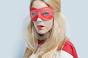 Portrait of a blond young woman wearing red eye mask against light blue background