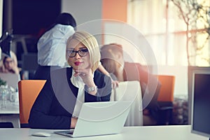 Portrait of a blonde female business partner in her 30`s sitting at her tidy desk in front of her computer.