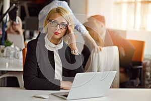 Portrait of a blonde female business partner in her 30`s sitting at her tidy desk in front of her computer.