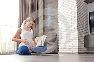 Portrait of blonde female sit on floor stroking big tummy with baby inside of it