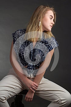 Portrait of blonde girl on a dark Studio background, he sits in the pose of Rodin`s thinker