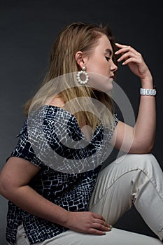 Portrait of blonde girl on a dark Studio background, he sits in the pose of Rodin`s thinker