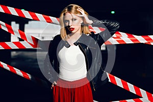 Portrait of blonde girl with red lips wearing a rock black style on the background of warning tape.