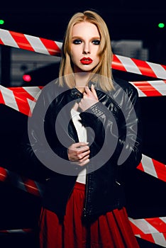 Portrait of blonde girl with red lips wearing a rock black style on the background of warning tape.
