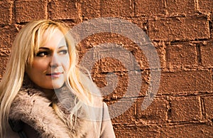 Portrait of blonde girl in warm coat over a brick wall