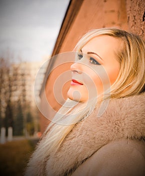 Portrait of blonde girl in warm coat over a brick wall