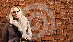 Portrait of blonde girl in warm coat over a brick wall