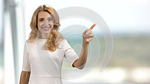 Portrait of a blonde mature happy woman pointing with her finger.